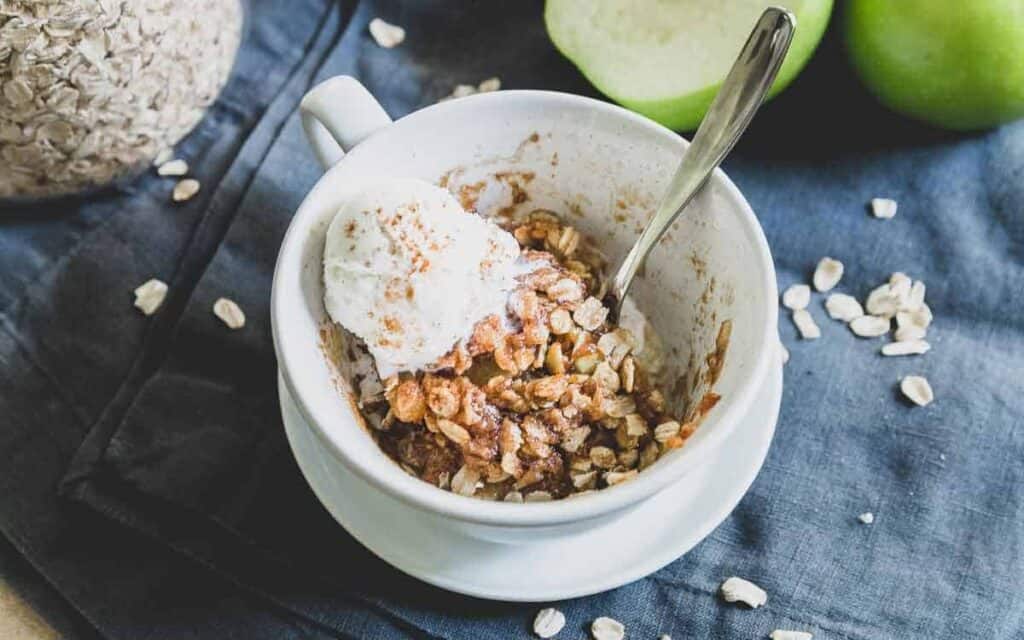 Apple crisp in a mug with ice cream and apples.