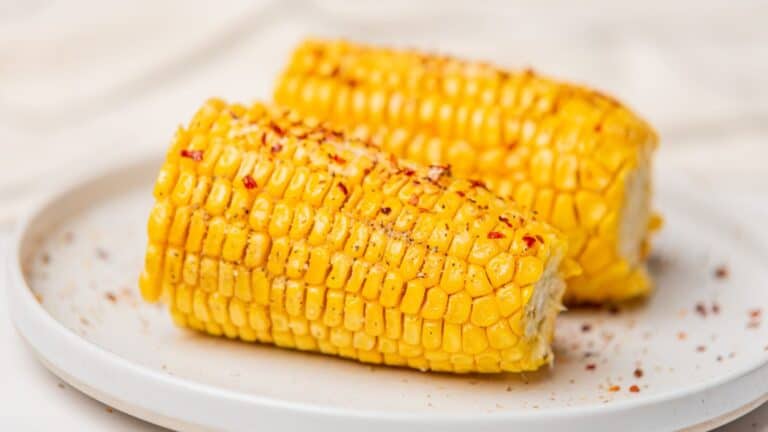 Two pieces of corn on the cob on a white plate.
