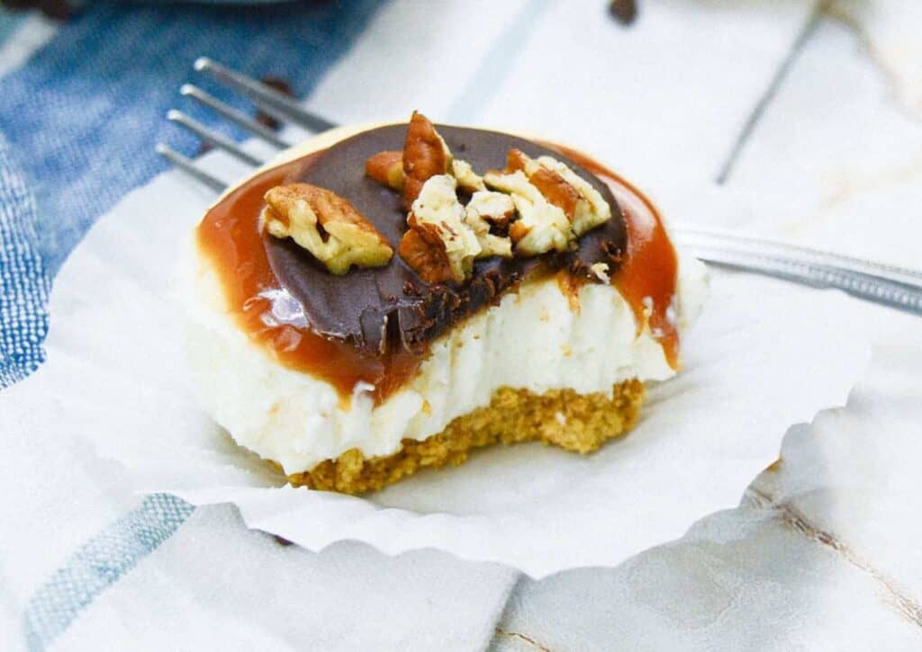 A slice of cheesecake with caramel and pecans on a plate.