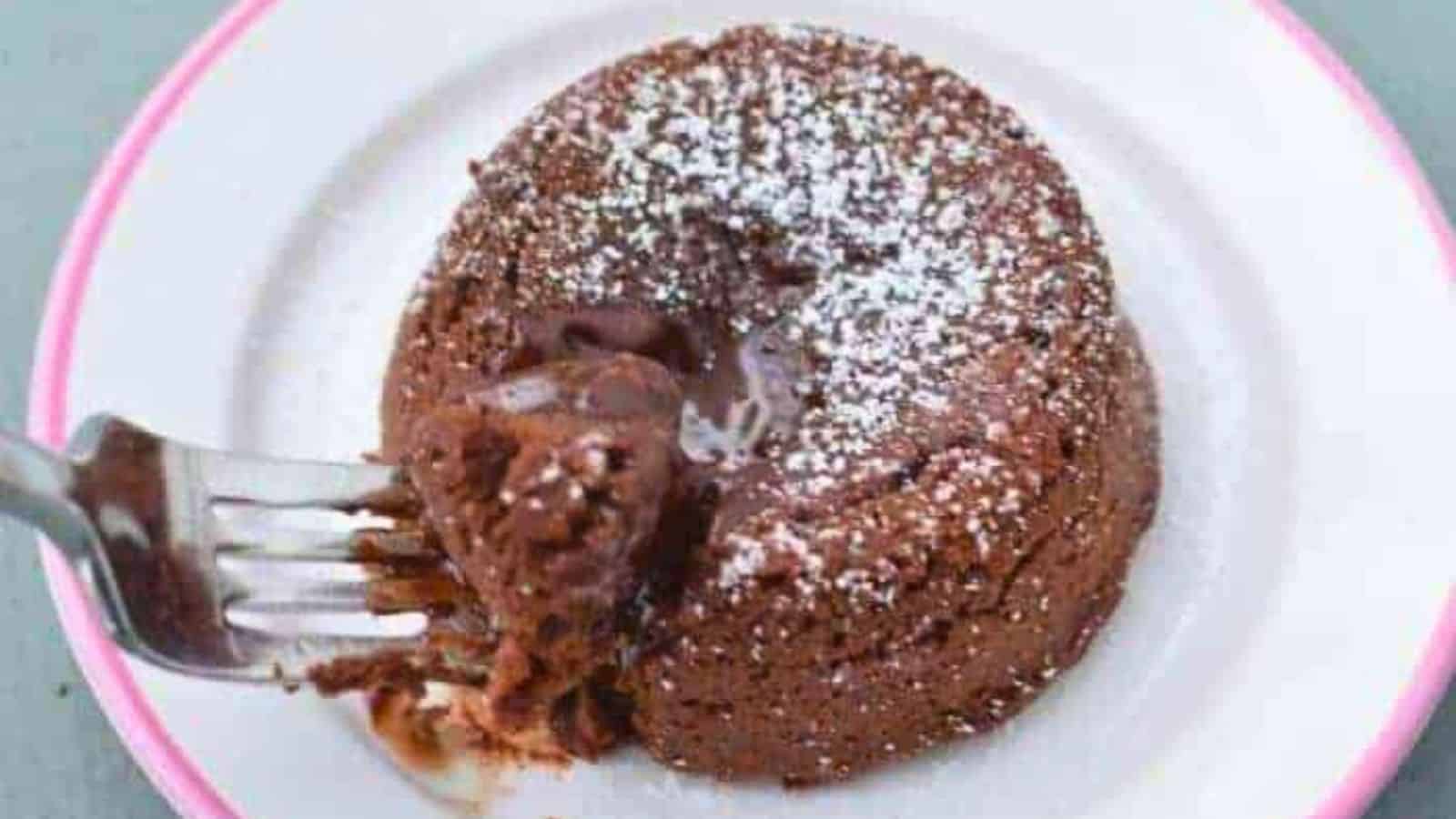 Image shows a fork pulling a bite from a molten chocolate cake on a white plate.