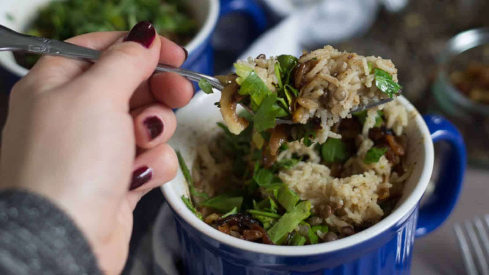 A person is holding a spoonful of rice in a blue mug.