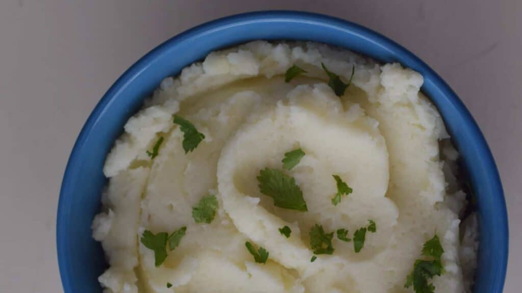 A bowl of mashed potatoes with parsley.