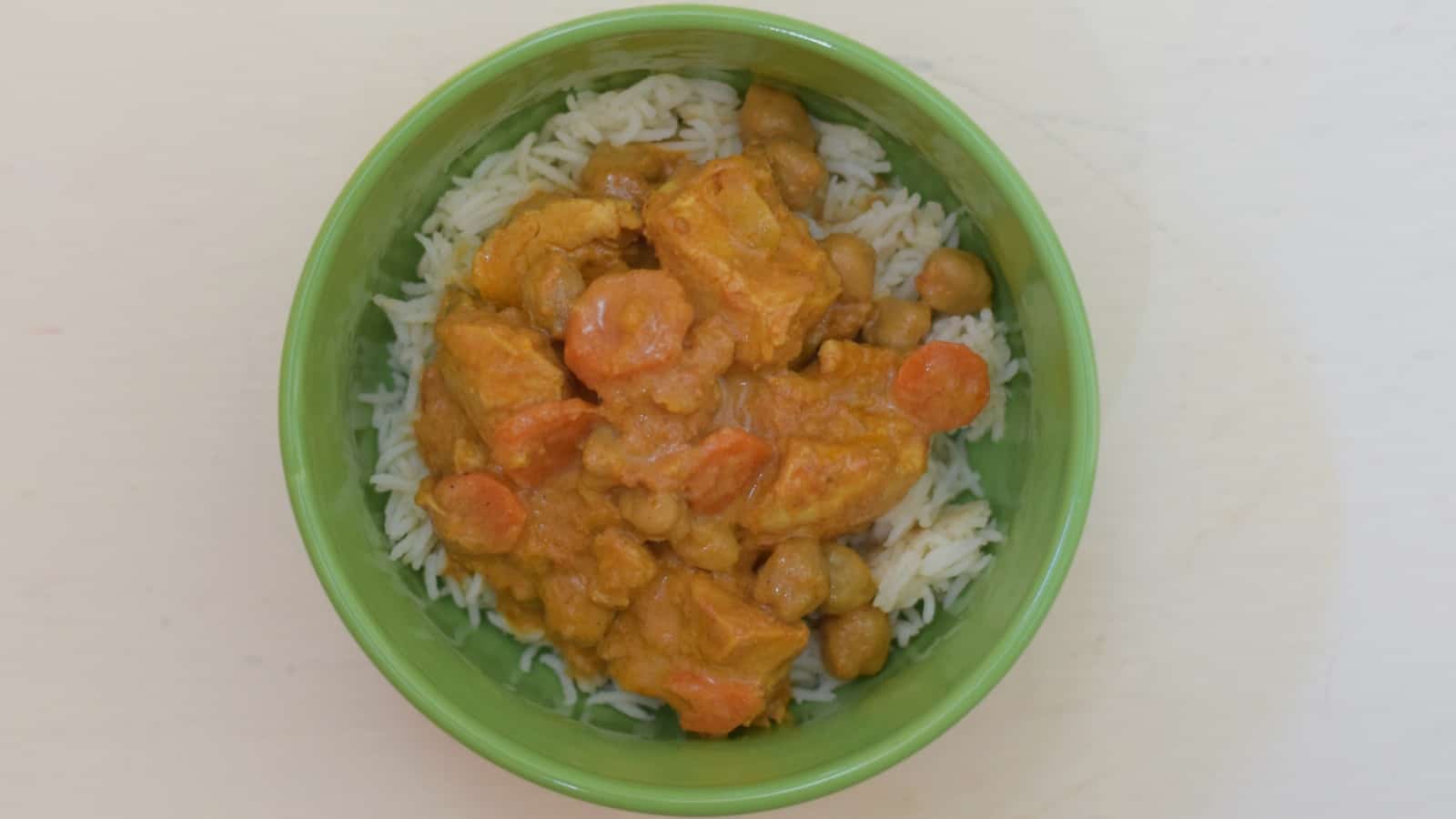 Overheat shot of chicken tikka masala in a green bowl on a white table.
