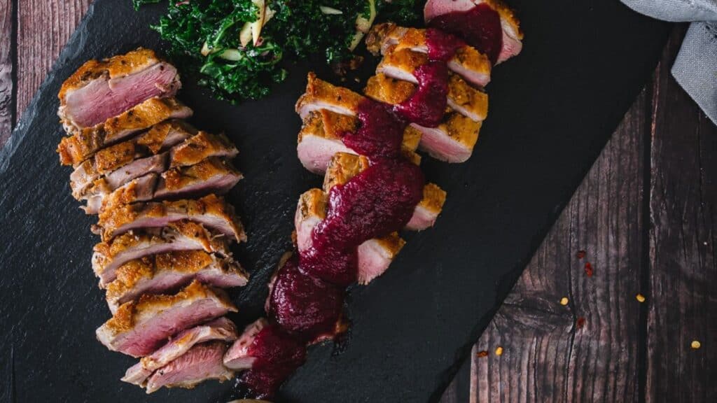 Overhead view of sliced duck breast with berry sauce.