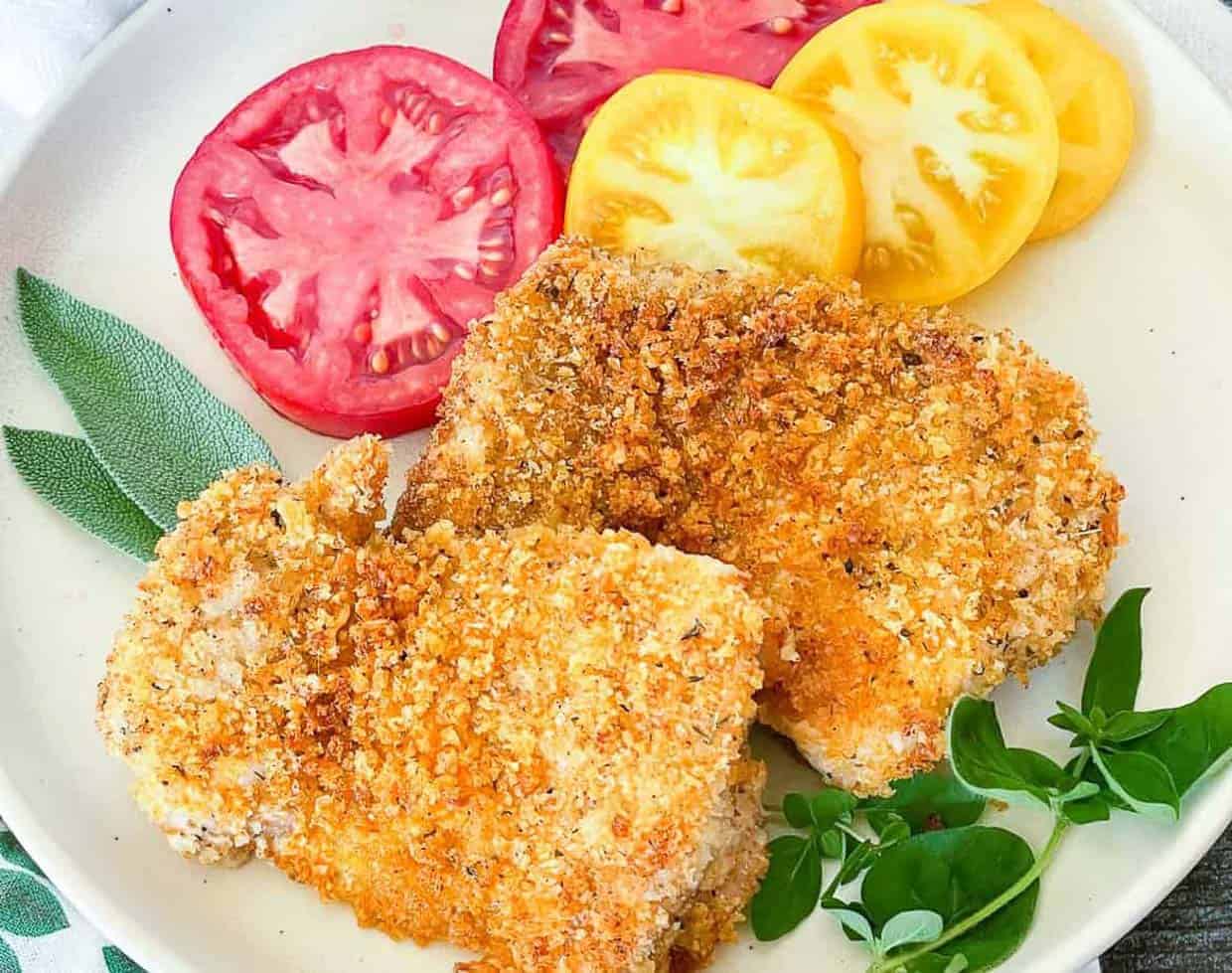 Panko chicken on a plate with tomato slices and fresh herbs.