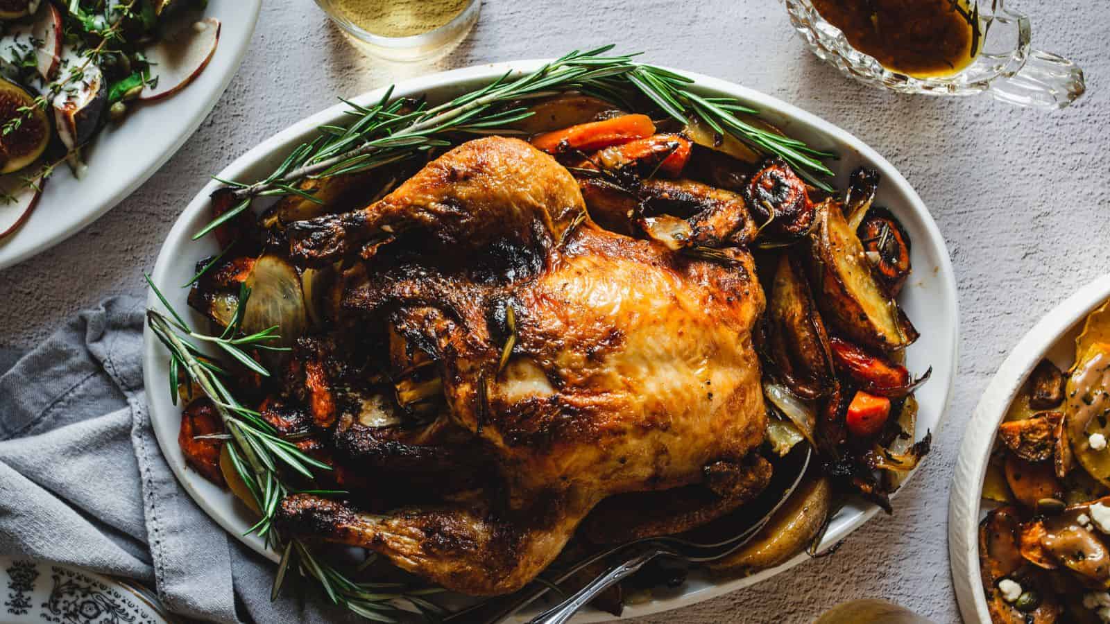 Hands holding paprika chicken and vegetables on a sheet pan.