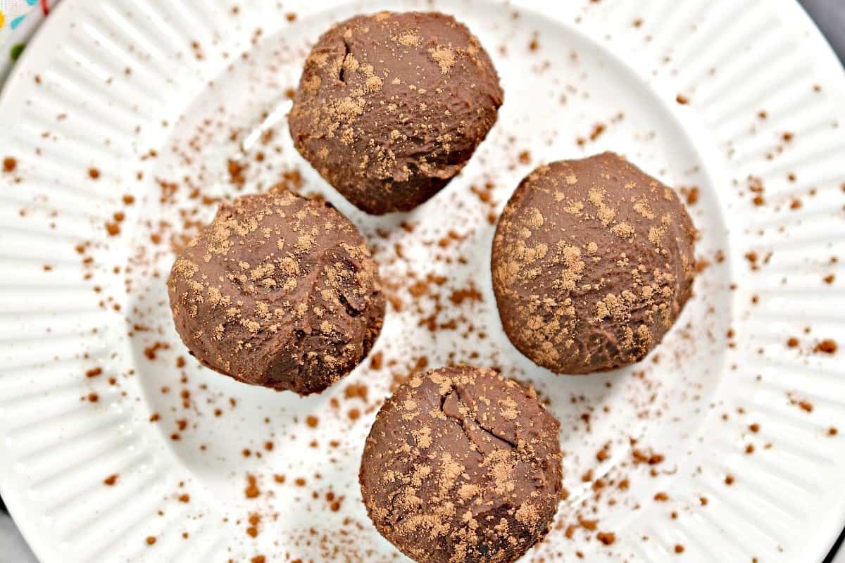 Four chocolate truffles on a white plate.