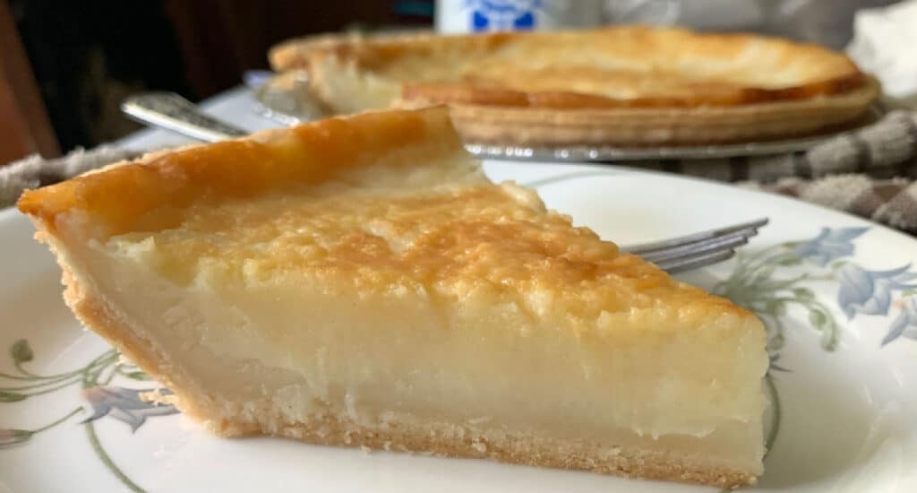 A slice of sugar cream pie on a plate with a fork.