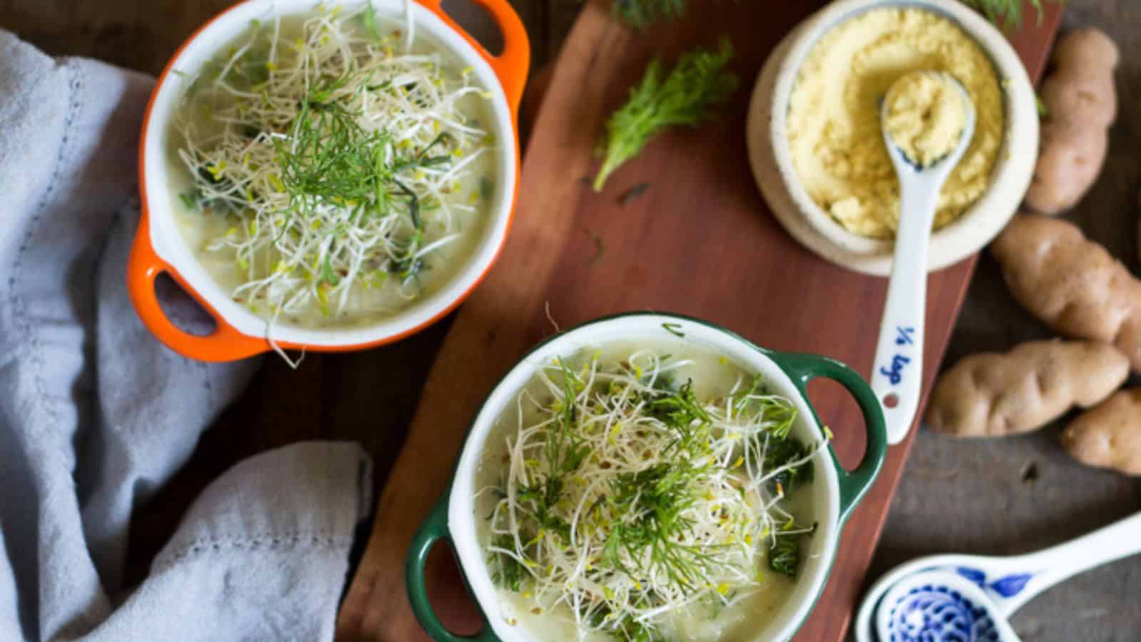 Two bowls of soup with dill on a wooden cutting board.