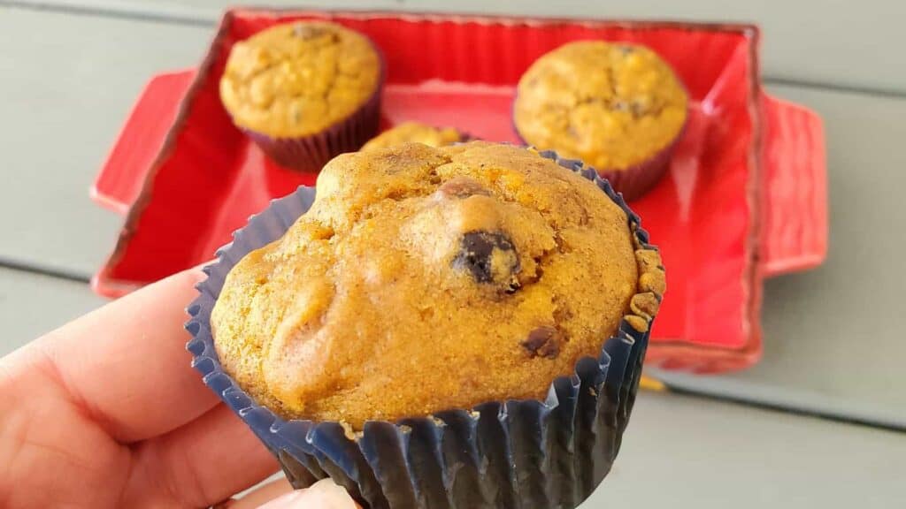 A person holding up a pumpkin muffin in a red tray.