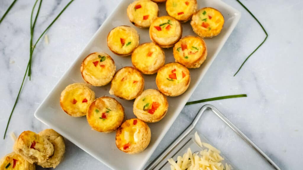 A white tray with mini swiss cheese quiches.