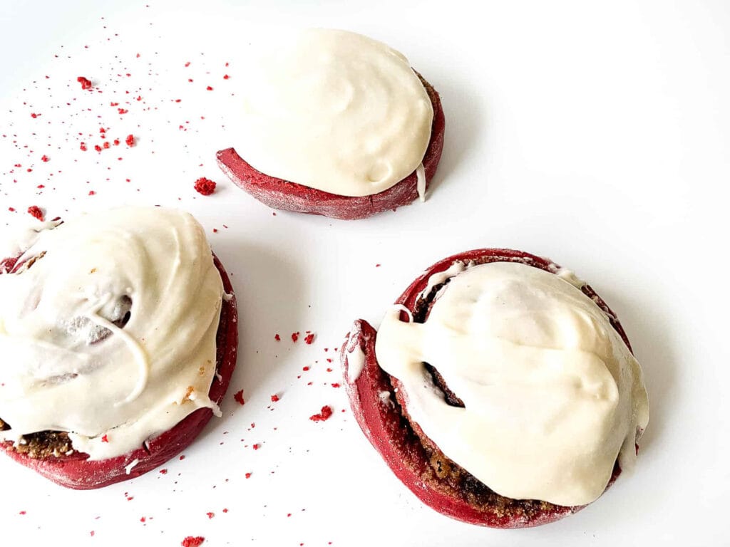 A plate with three red velvet cinnamon rolls with icing on top, perfect for dessert.