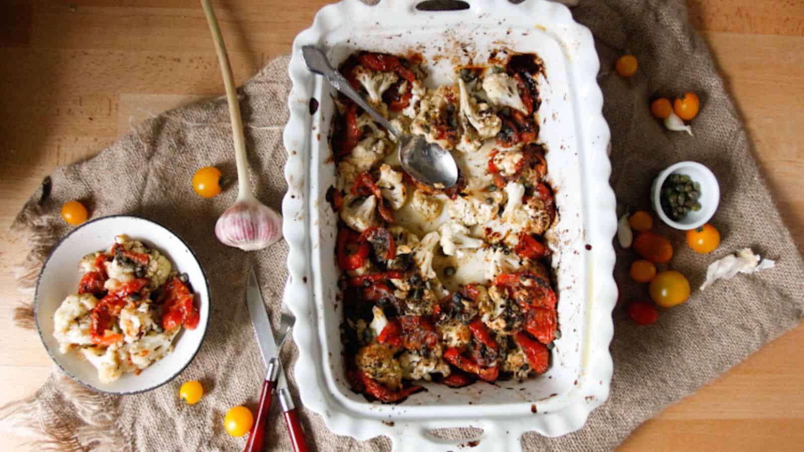 A veggie casserole dish with tomatoes and herbs on a table.