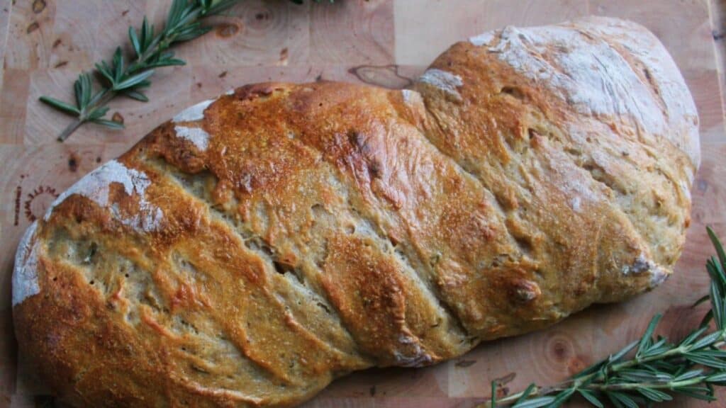 Bread loaf on cutting board with rosemary.
