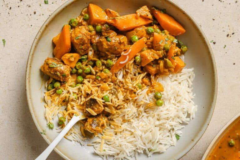 A bowl of rice and sausage curry on a table.