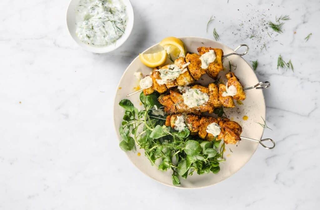 Chicken kebabs with tzatziki sauce on a white plate.