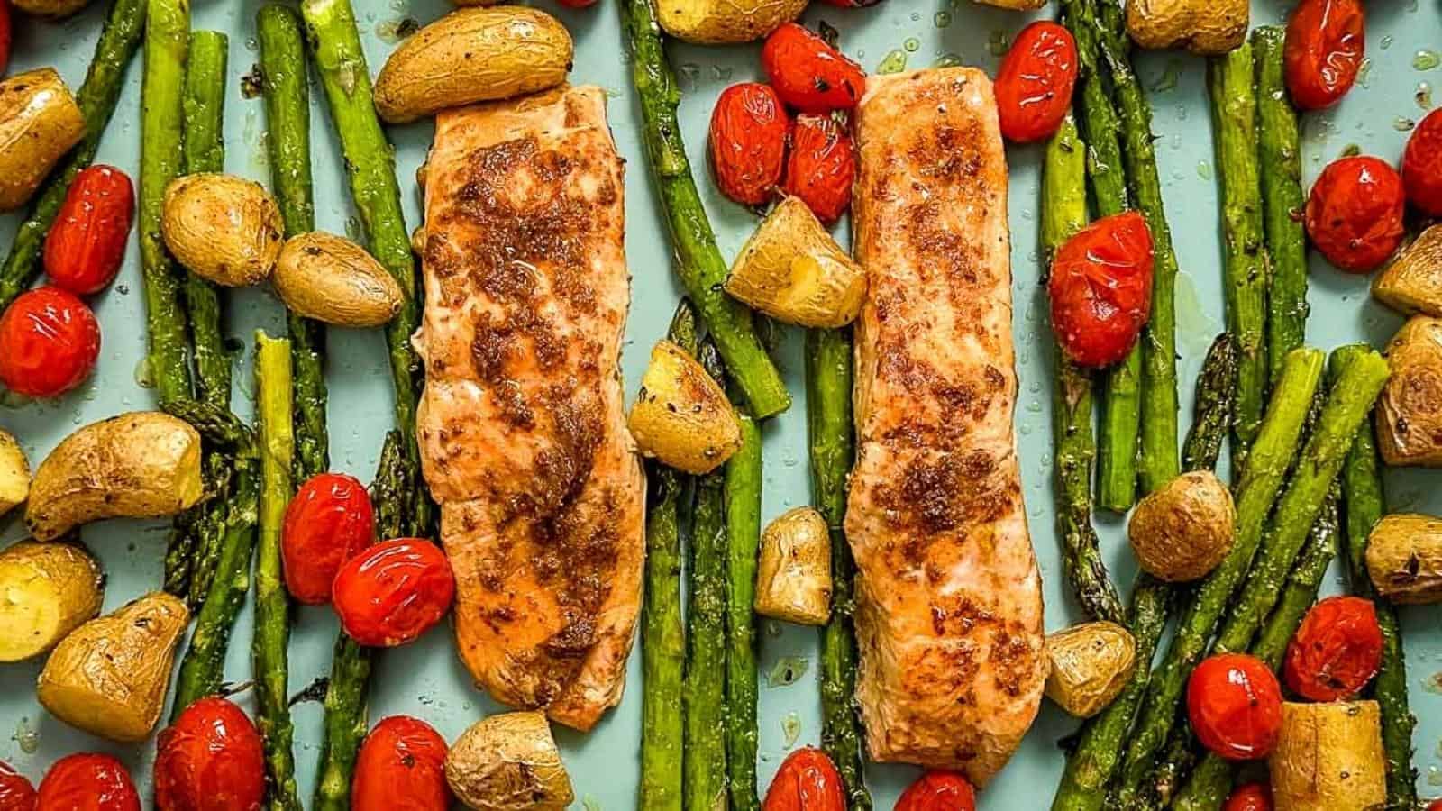 Closeup overhead shot of roasted salmon, asparagus, fingerling potatoes, and cherry tomatoes on a blue sheet tray.