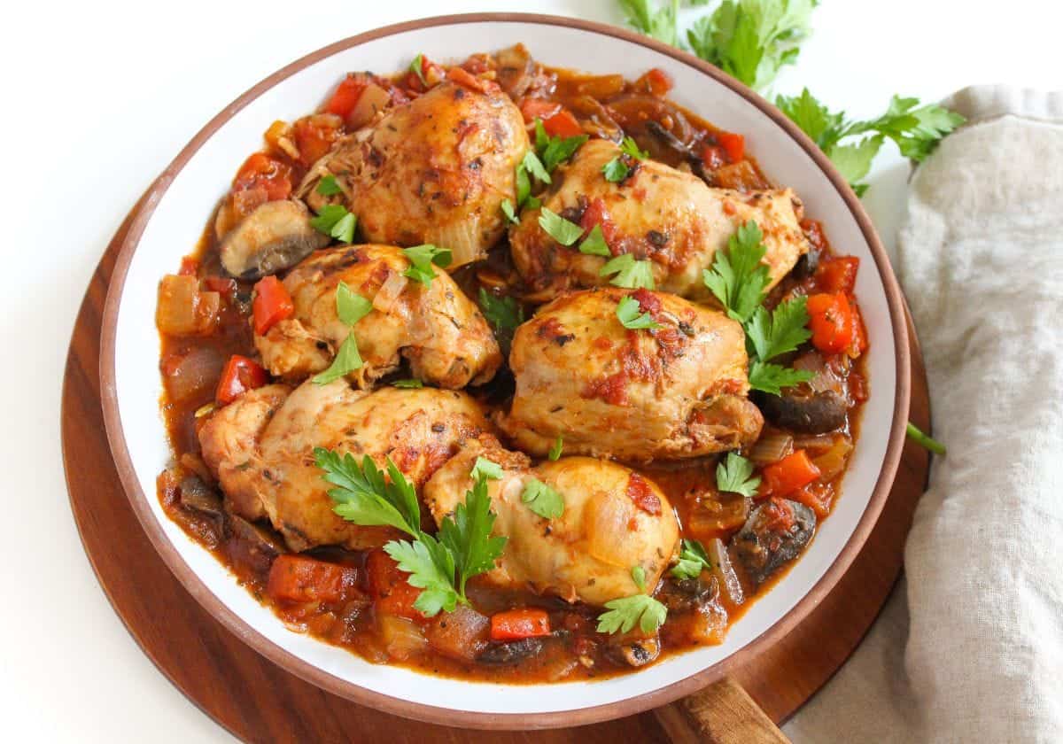 Chicken thighs in tomato sauce on a large white plate.