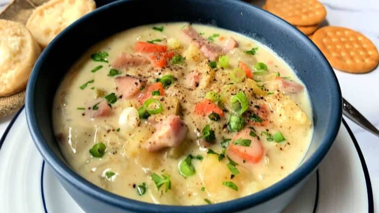 A bowl of ham chowder with crackers on a plate.