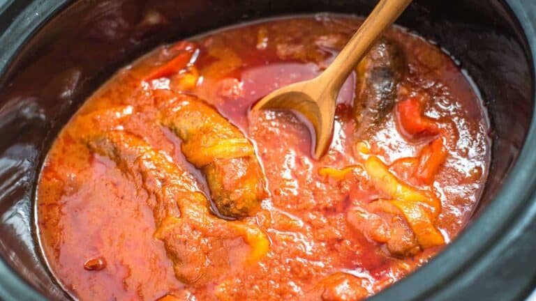 A crock pot full of meat and sauce with a wooden spoon.