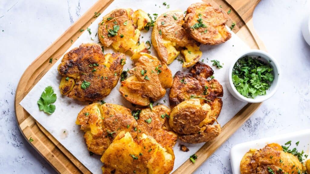 Smashed potatoes on a cutting board with parsley.