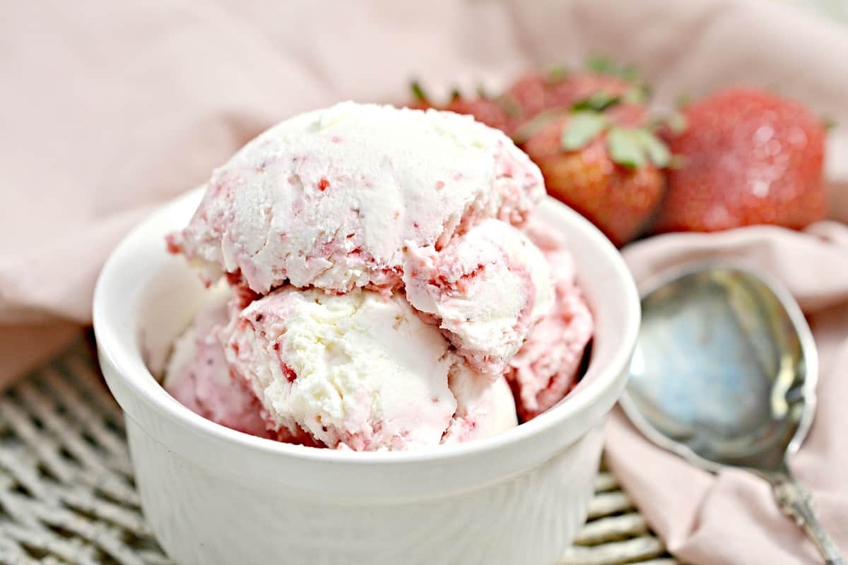 Strawberry ice cream in a bowl with a spoon.