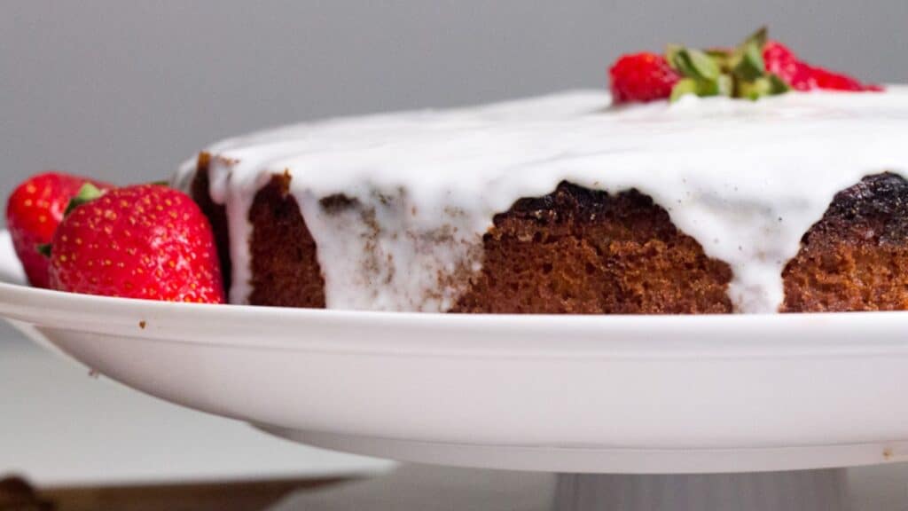 A cake with icing and strawberries on a white plate.