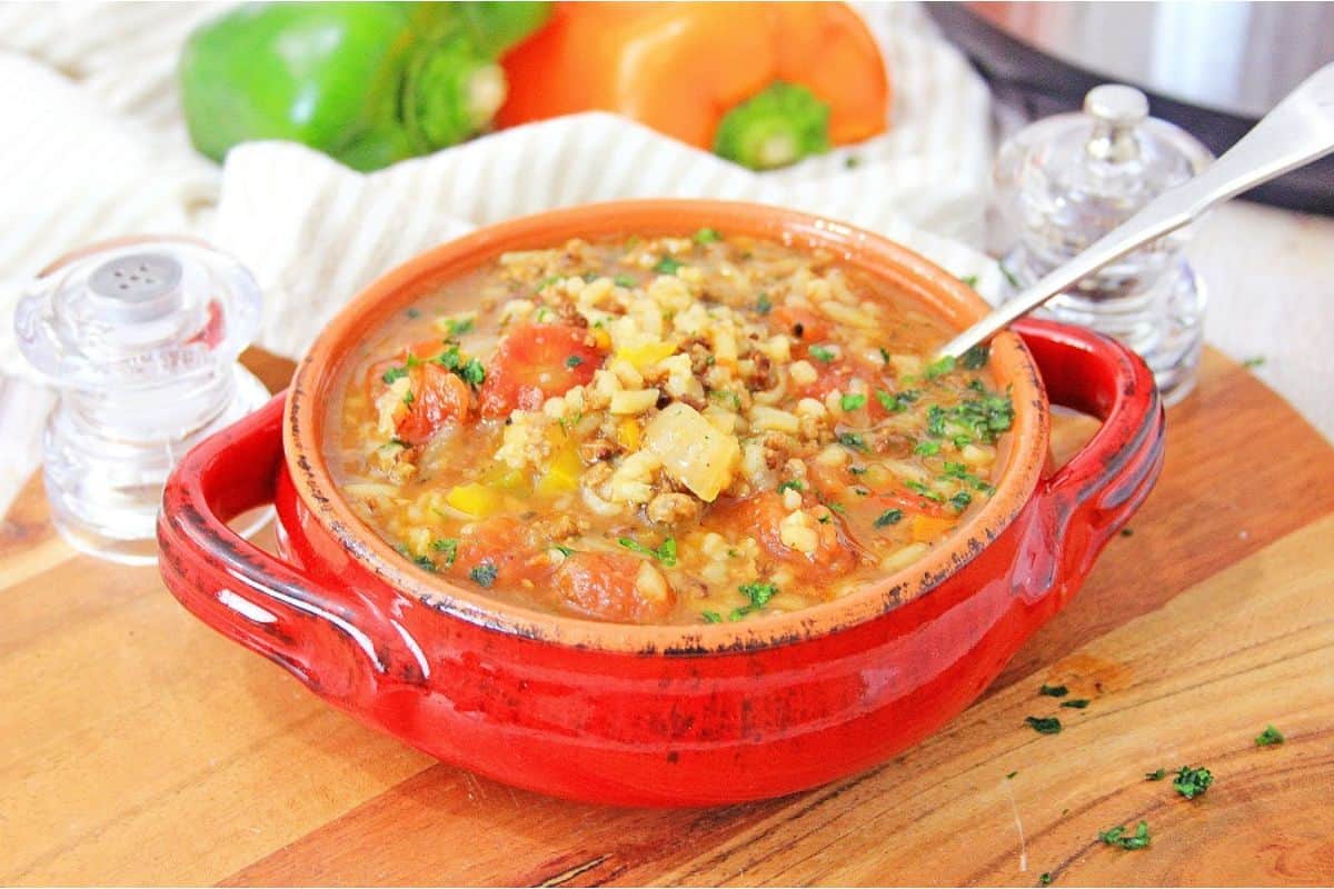 A red bowl of soup with a spoon on a wooden cutting board.