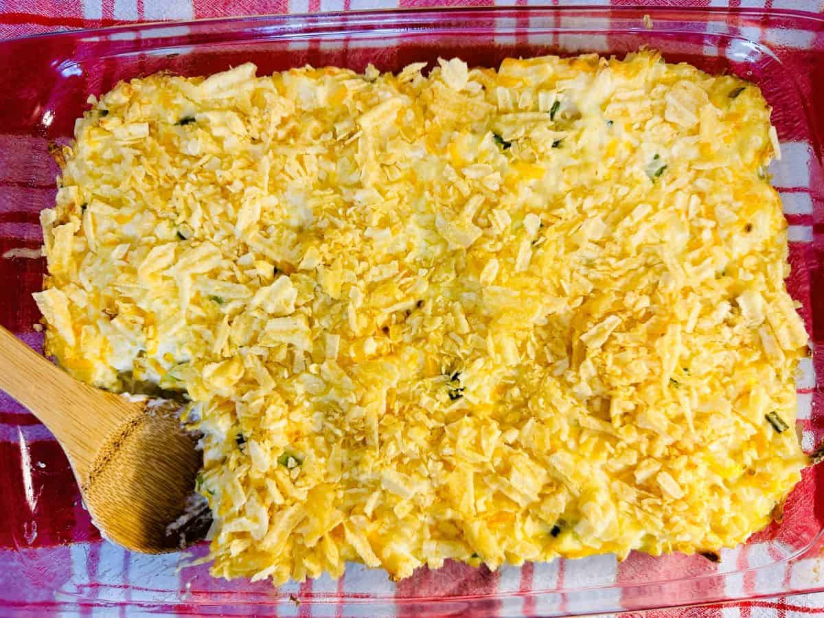 A casserole dish with shredded cheese and a wooden spoon.