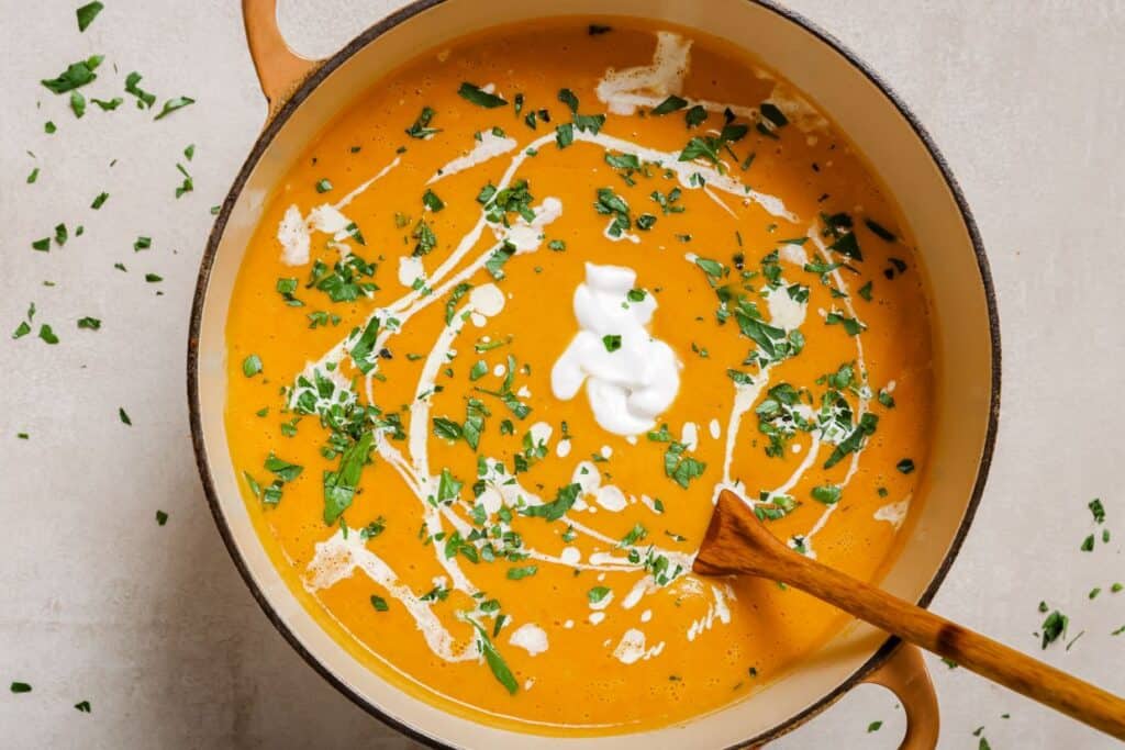 A pot of sweet potato and red pepper soup with sour cream and parsley.