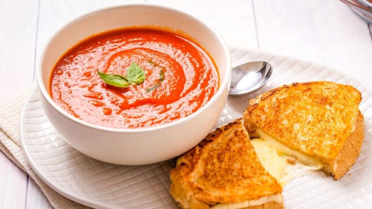 A bowl of tomato soup with a slice of grilled cheese.