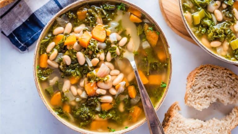 A bowl of kale and bean soup with bread.