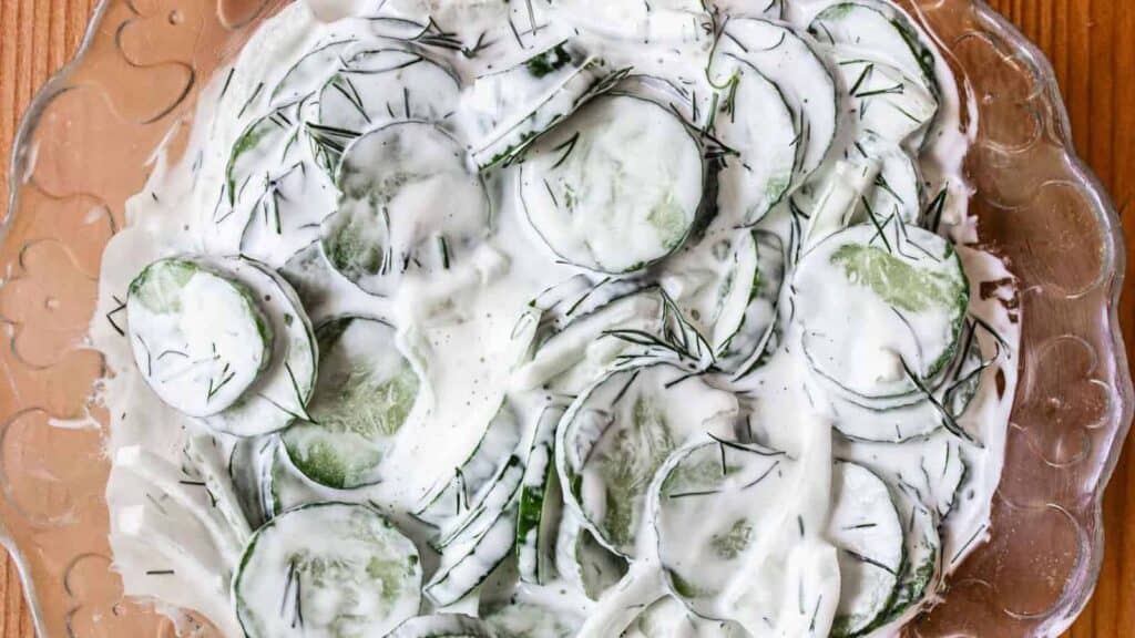 A glass bowl filled with cucumbers and cream.