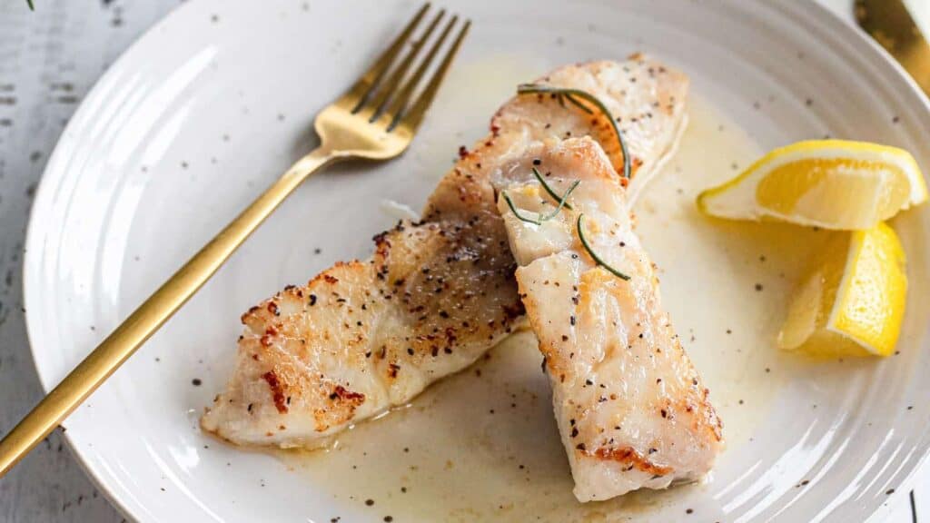 Two pieces of fish on a plate with lemon slices and a fork.