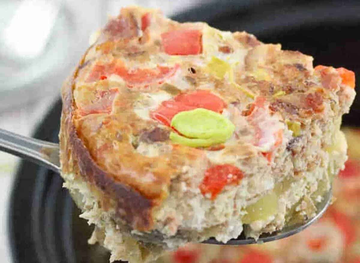 Dairy-free egg casserole with peppers and leeks in a black slow cooker with a steel spoon in it.