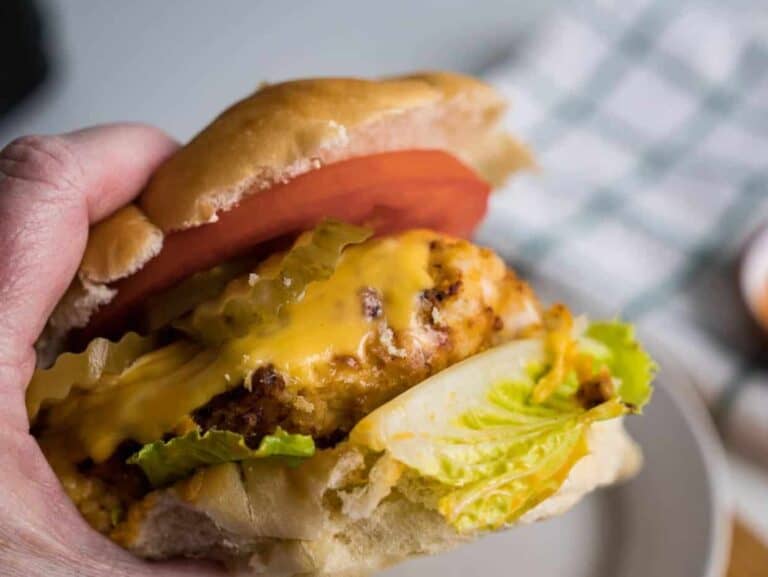 A person holding a chicken burger with cheese and lettuce.