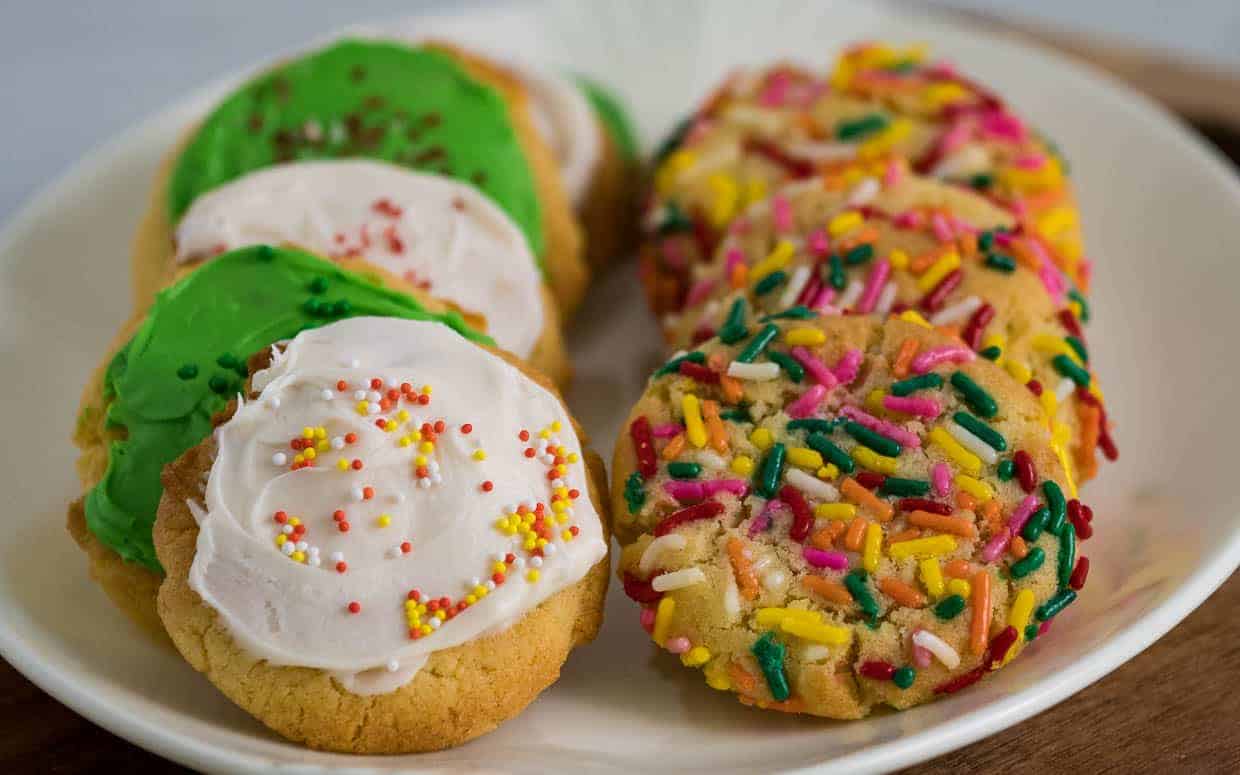 Sugar cookies with frosting and sprinkles on a white plate.