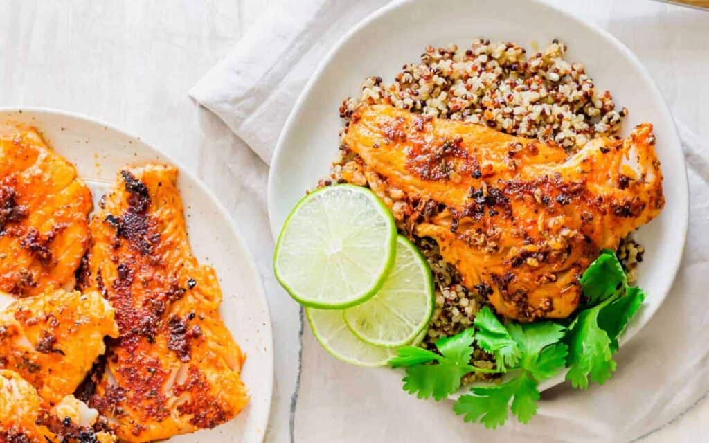 A plate of blackened cod with rice and lime wedges.