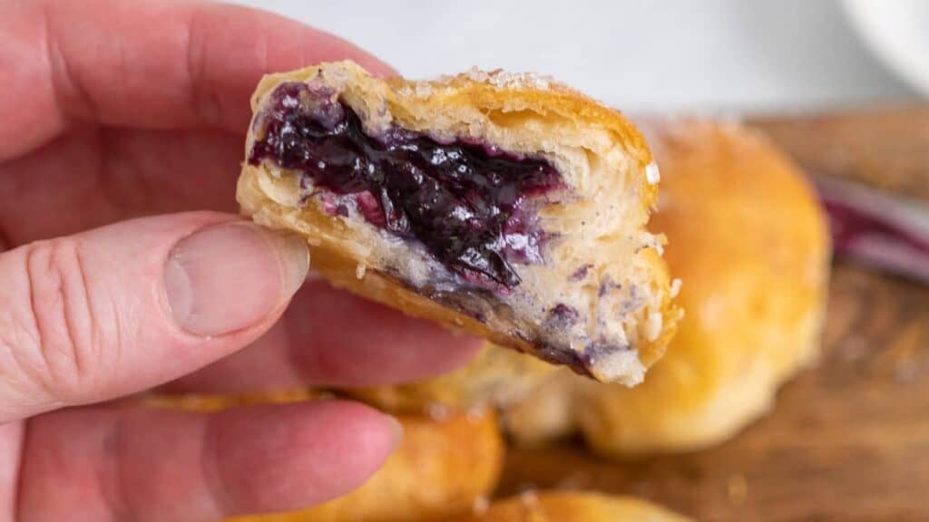 A person holding a pastry with blueberry filling.