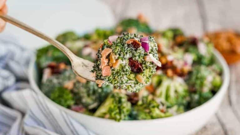 A person is holding a spoonful of broccoli salad.