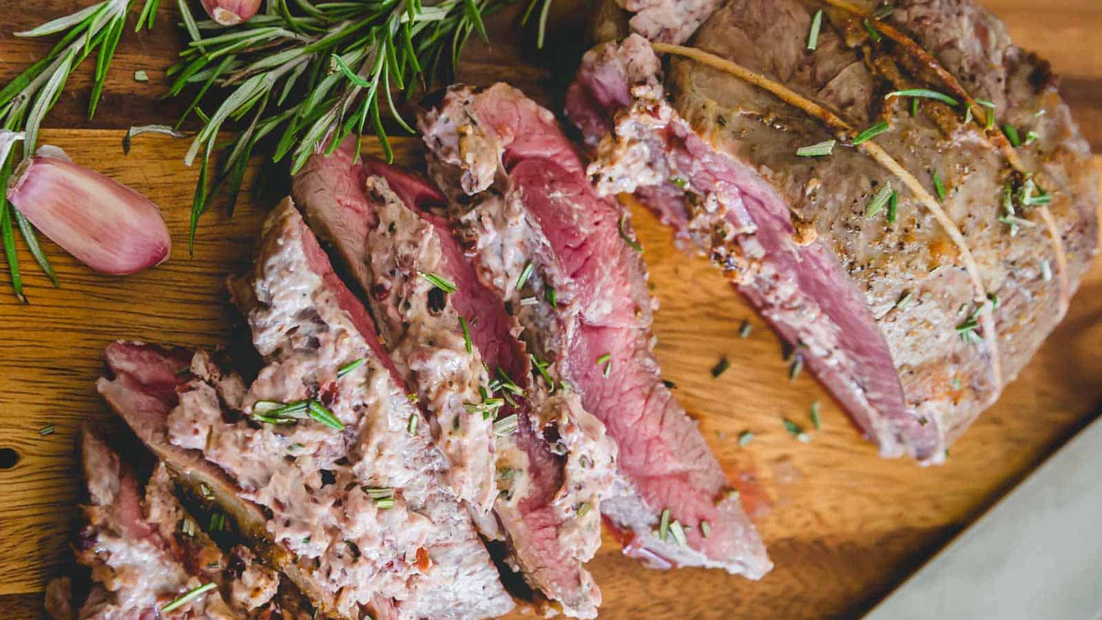 Butterflied lamb on a wooden cutting board with rosemary sprigs and cranberry goat cheese filling.