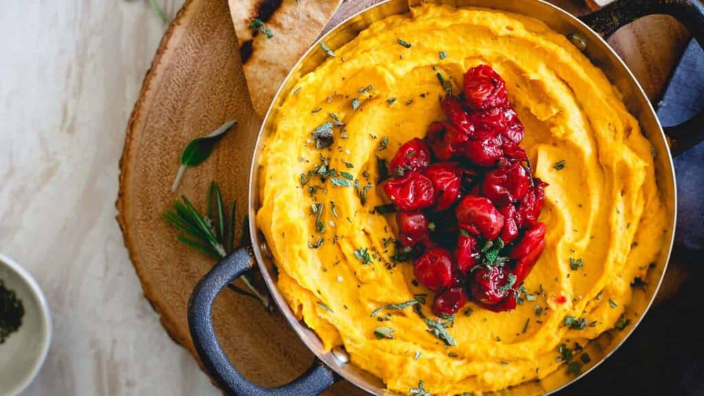 A bowl of butternut squash goat cheese dip with cherries.