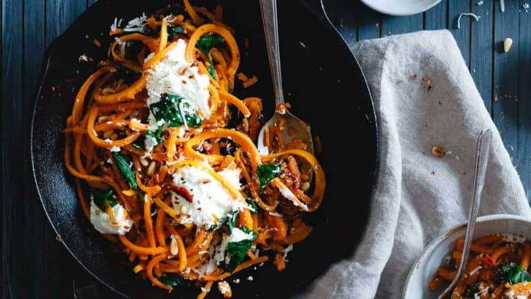 A skillet full of butternut squash spaghetti with spinach and ricotta cheese.