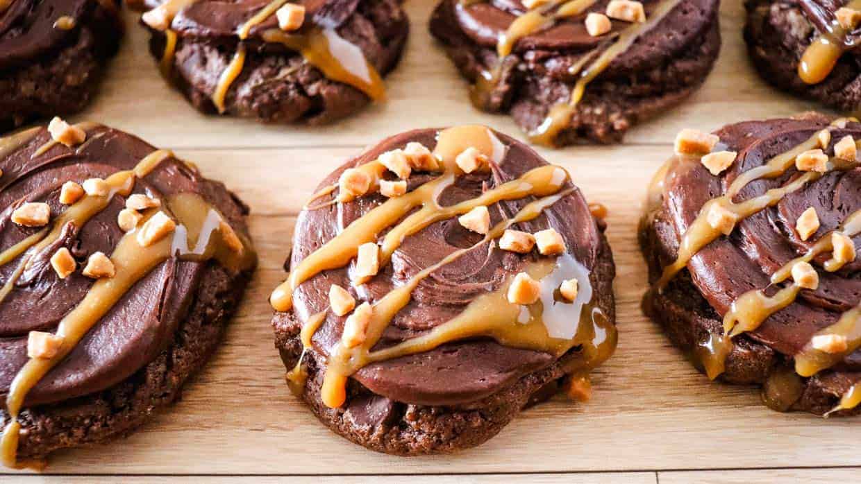 Chocolate caramel cookies on a cutting board topped with nuts and caramel.