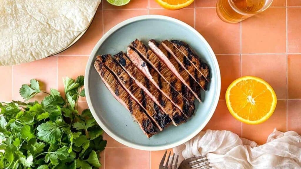 A plate with a grilled steak and oranges on it.