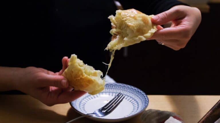 Hands pulling two halves of a cheese empanada.