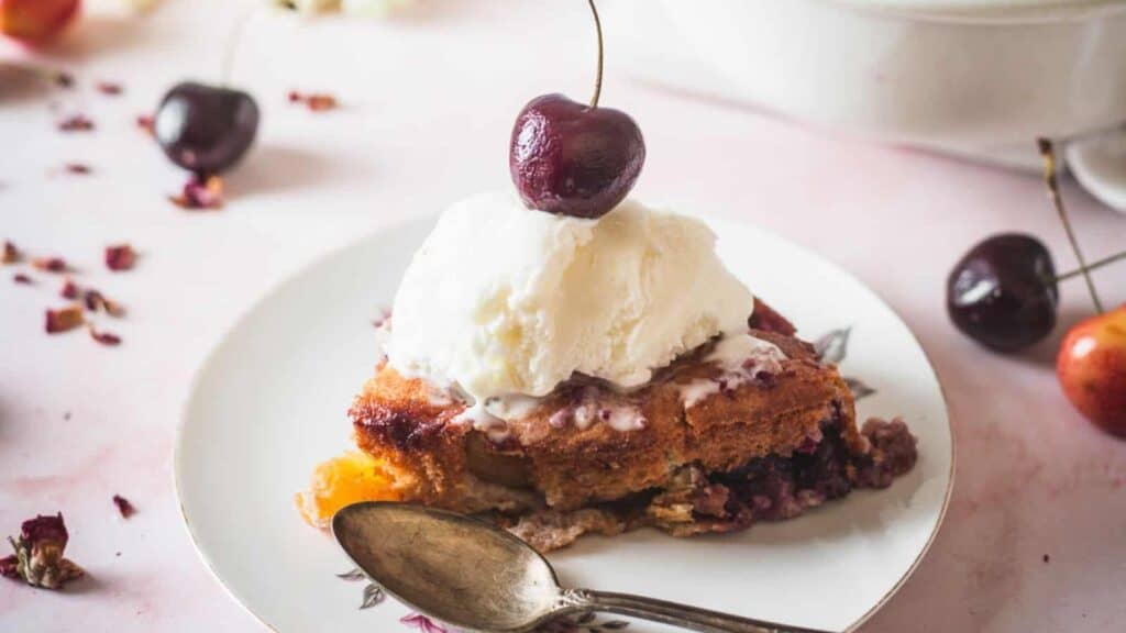 A fruit dessert featuring a piece of cake with ice cream and cherries on top.