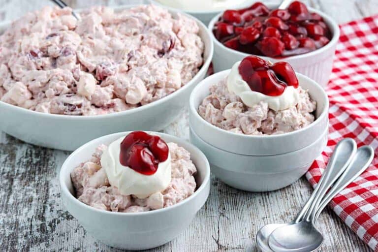 A bowl of cranberry salad with whipped cream and cherries.