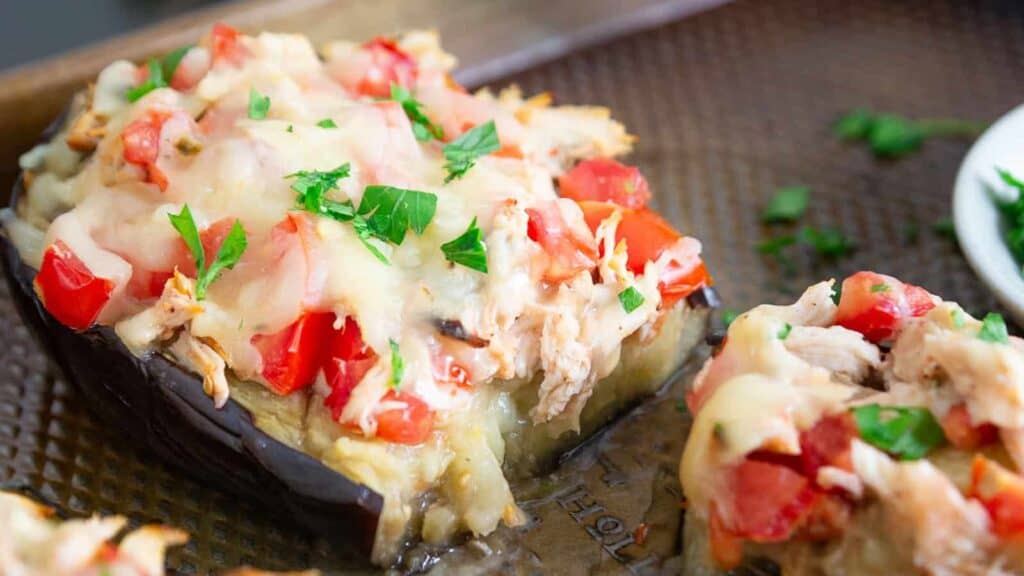 Eggplant stuffed with chicken and tomatoes on a baking sheet.
