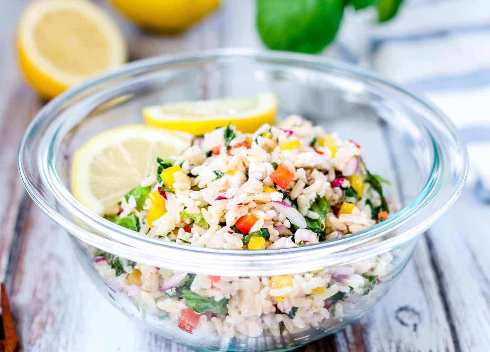 A bowl of rice salad with lemon and lemon wedges.